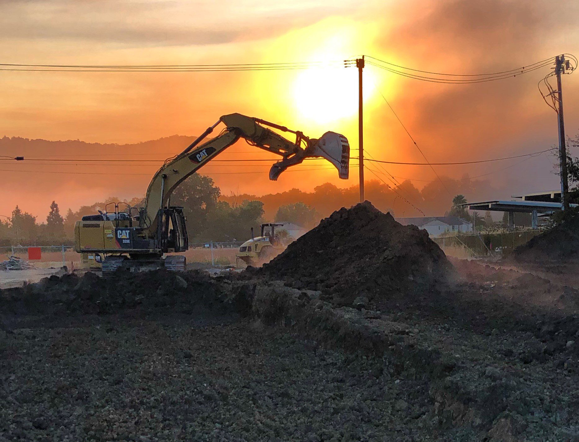 Excavator working at sunset with dramatic lighting and smoke.